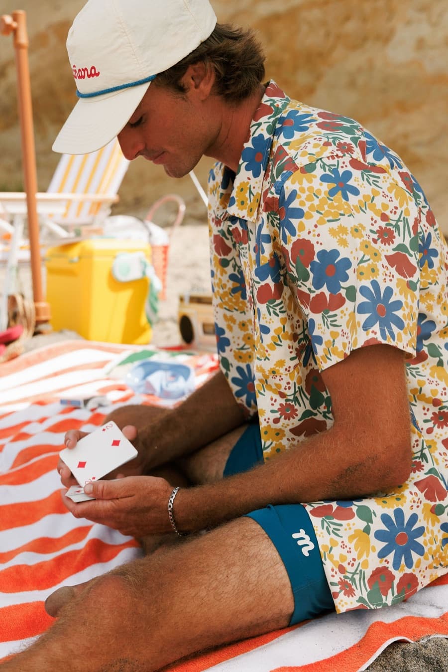 Playing cards on a striped beach towel in a floral Breeze shirt