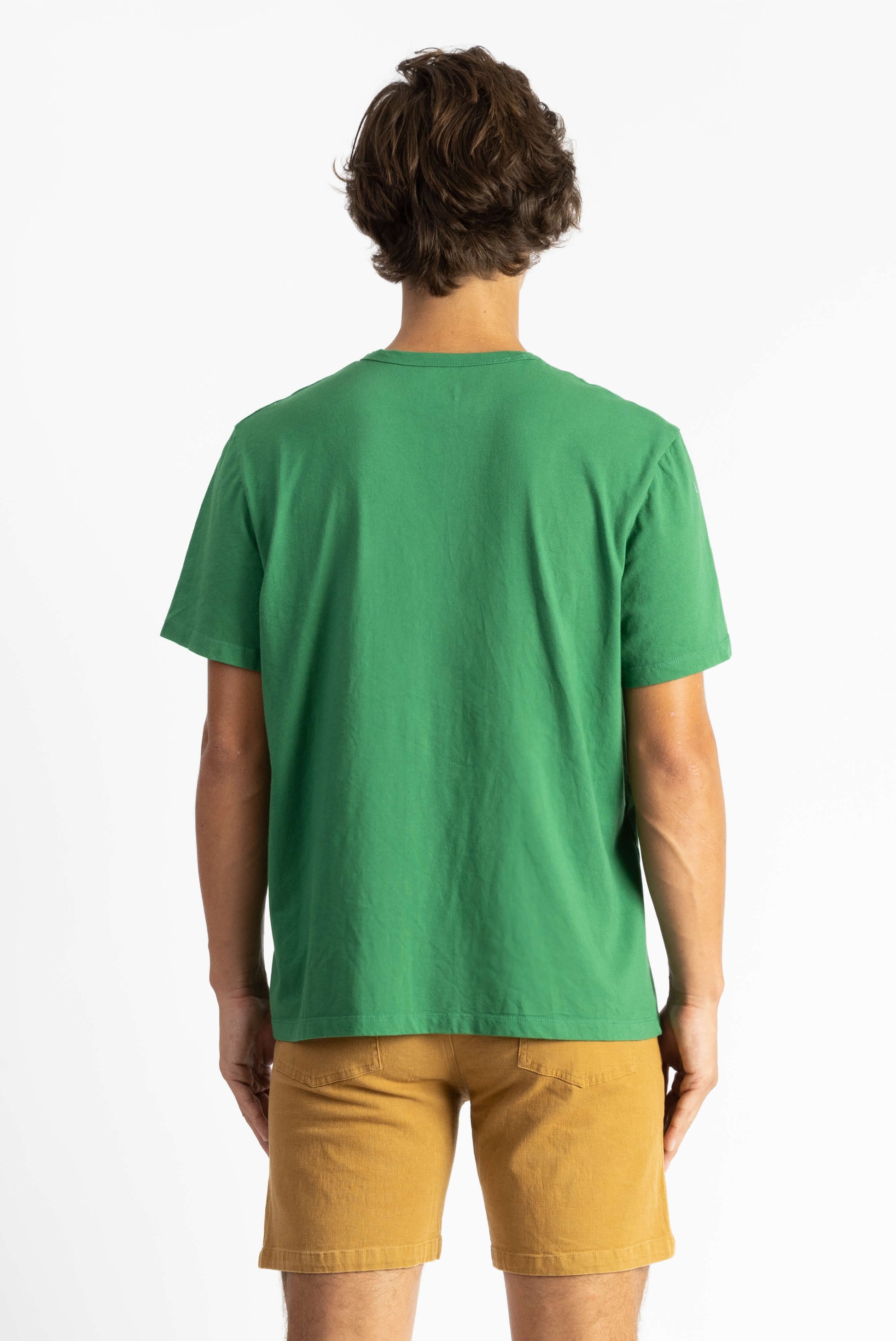 A man wearing a Green Workshop Tee Shirt having Manana branding with golden shorts