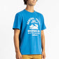 A man wearing a Swedish Blue Workshop Tee Shirt having Manana branding with golden shorts