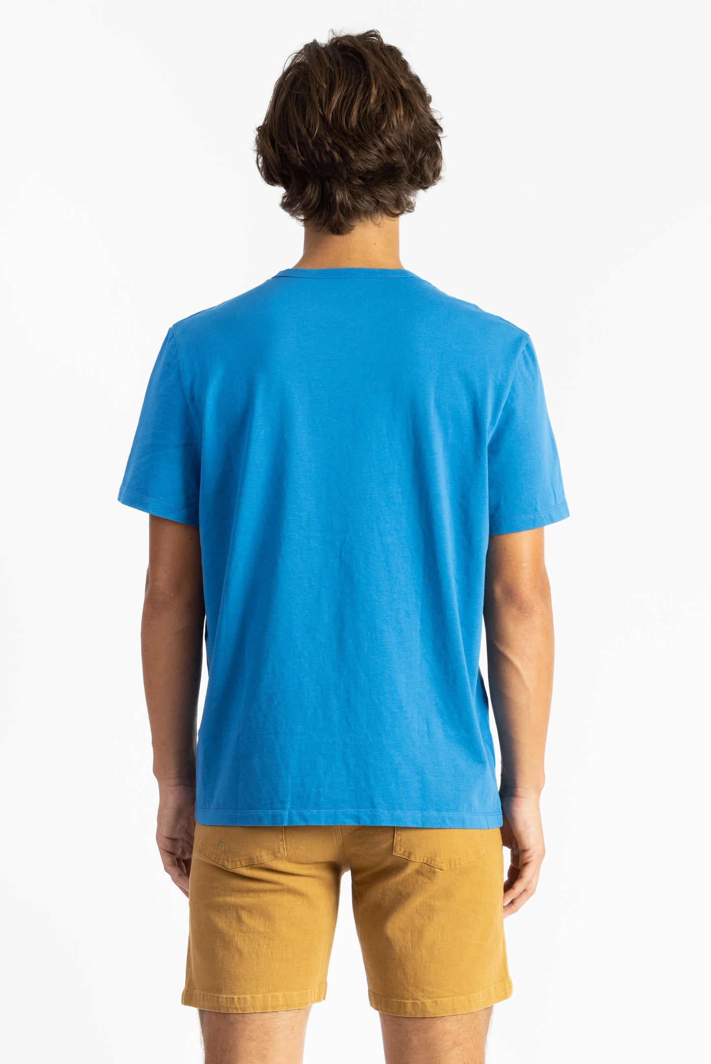 A man wearing a Swedish Blue Workshop Tee Shirt having Manana branding with golden shorts