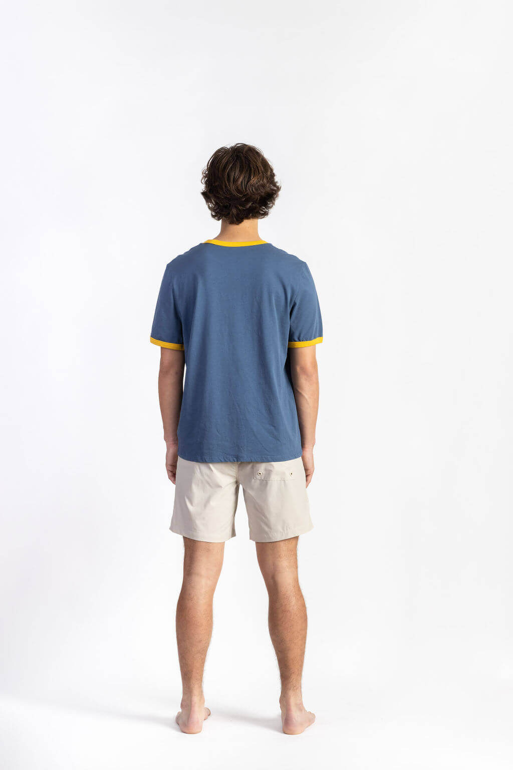 A man wearing a blue summer tee shirt having manana branding with white shorts