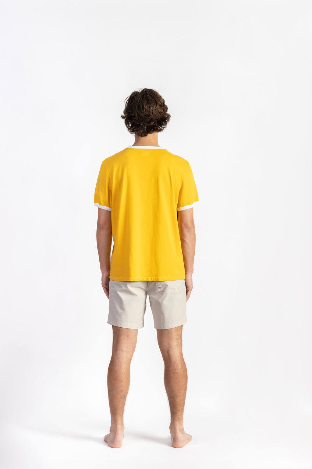 A man wearing a Yellow Logo Ringer Shirt having Manana branding with white shorts